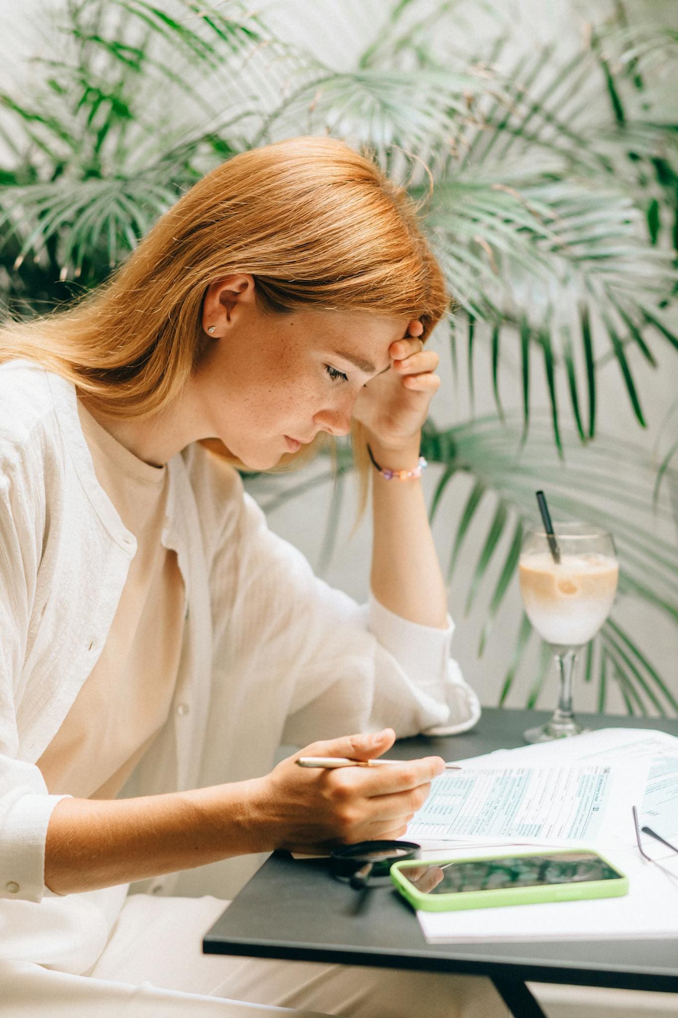 Focused woman reviewing documents in a cafe setting, enjoying a drink.
